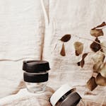 Stylish glass coffee cups with black lids on rustic fabric, emphasizing sustainability.