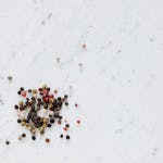 Top view of heap of assorted whole peppers on smooth marble light surface